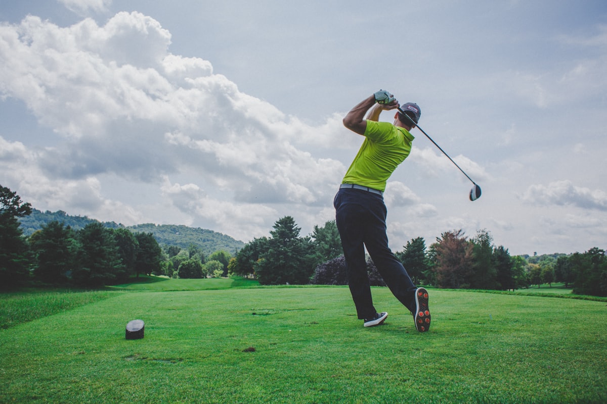 A golfer finishing a drive from an elevated tee on an open fairway